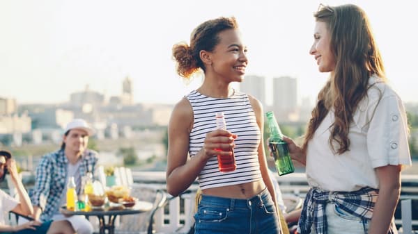Two friends laughing together with drinks at golden hour